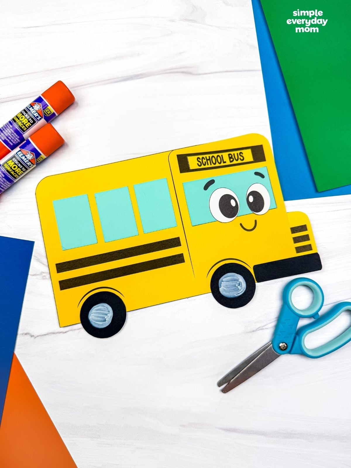 A completed craft showing the finished bus shape craft with colorful paper, scissors, and glue sticks nearby.