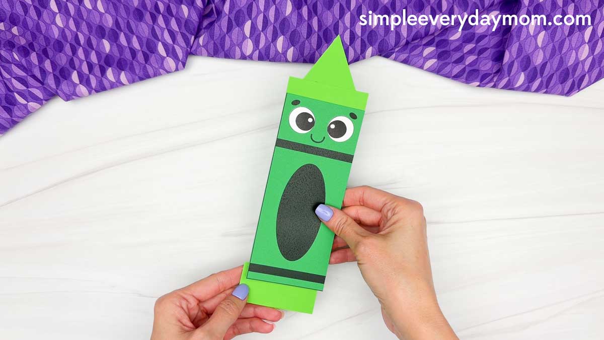 Hands holding the completed crayon shape craft while sliding the bottom piece to reveal the hidden color.