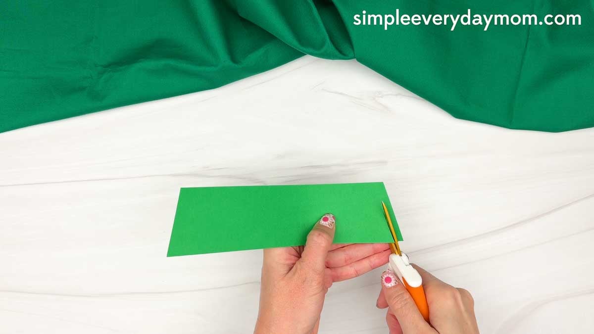 Hands cutting a long strip of paper to make the backing for the thankful pumpkin craft.