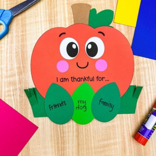 A completed craft of the thankful pumpkin with gratitude leaf inserts displayed alongside colorful craft supplies.