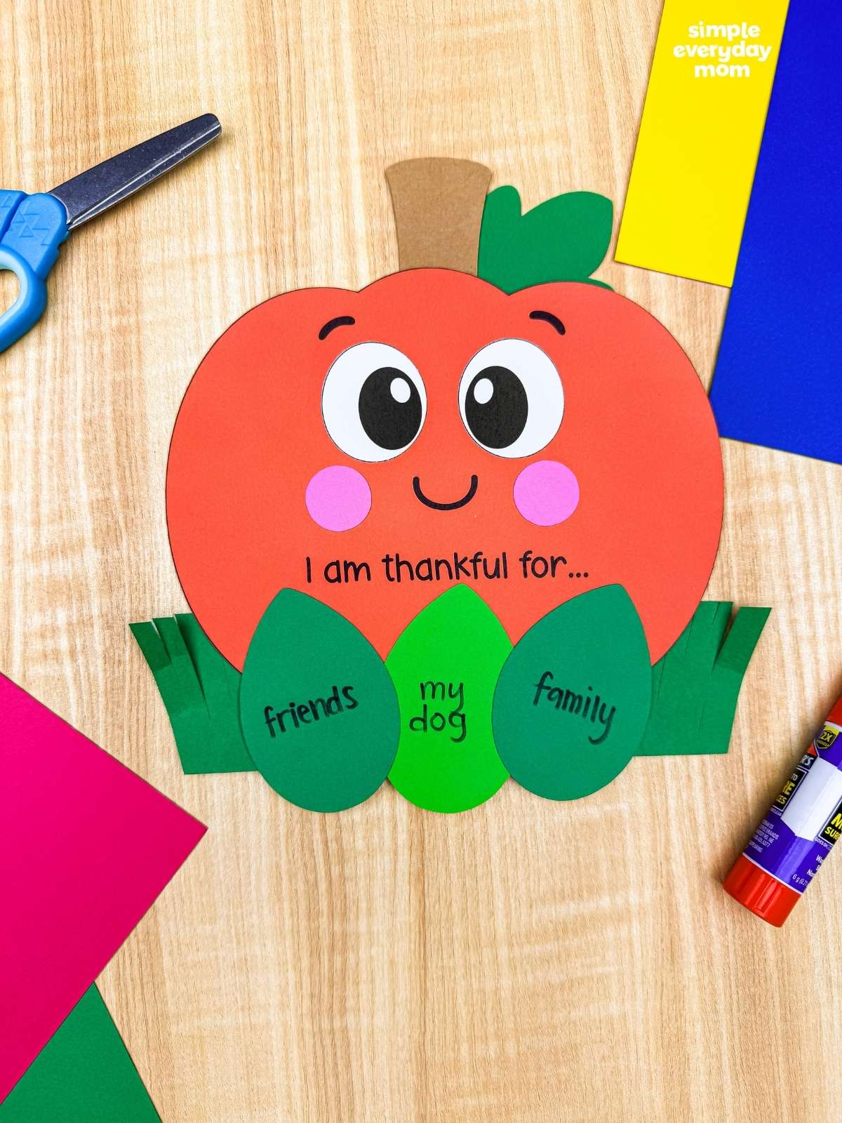 A completed craft of the thankful pumpkin with gratitude leaf inserts displayed alongside colorful craft supplies.
