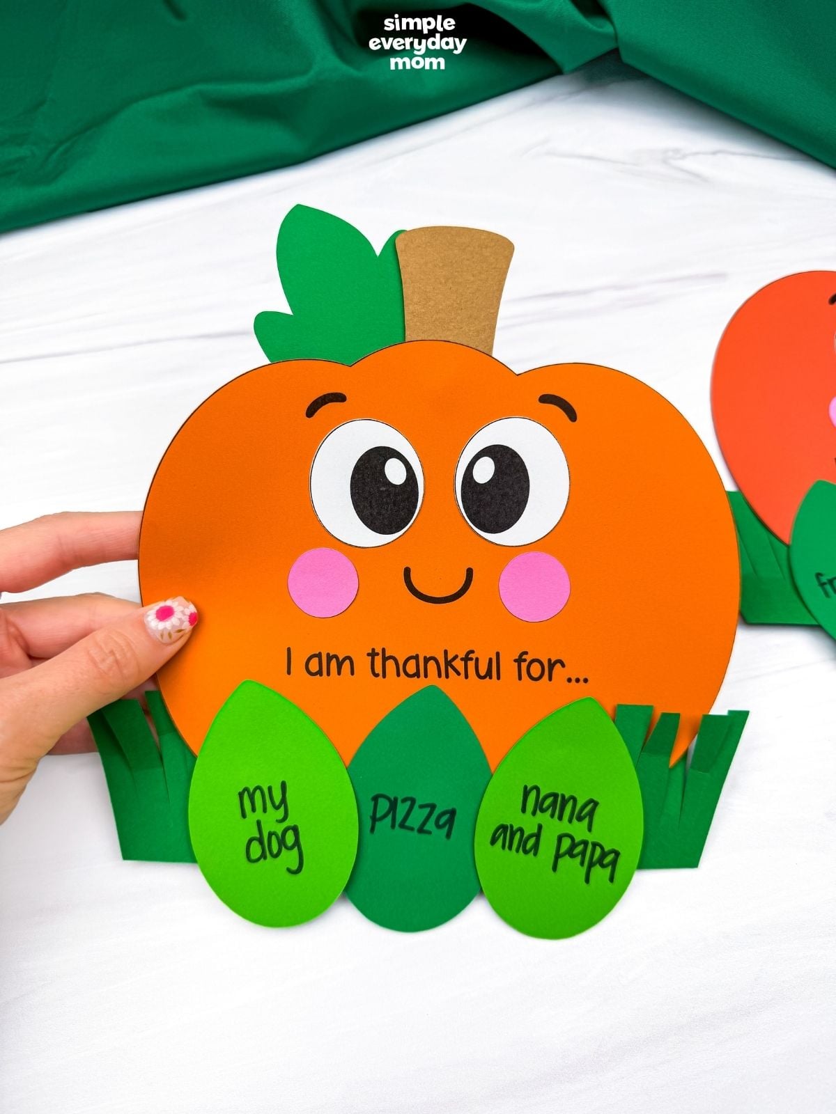 Hands holding the completed thankful pumpkin craft with gratitude leaf inserts tucked into the grass pockets.