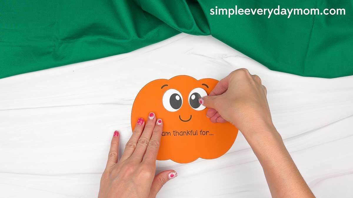 Hands gluing the right cheek onto the thankful pumpkin face below the eye.