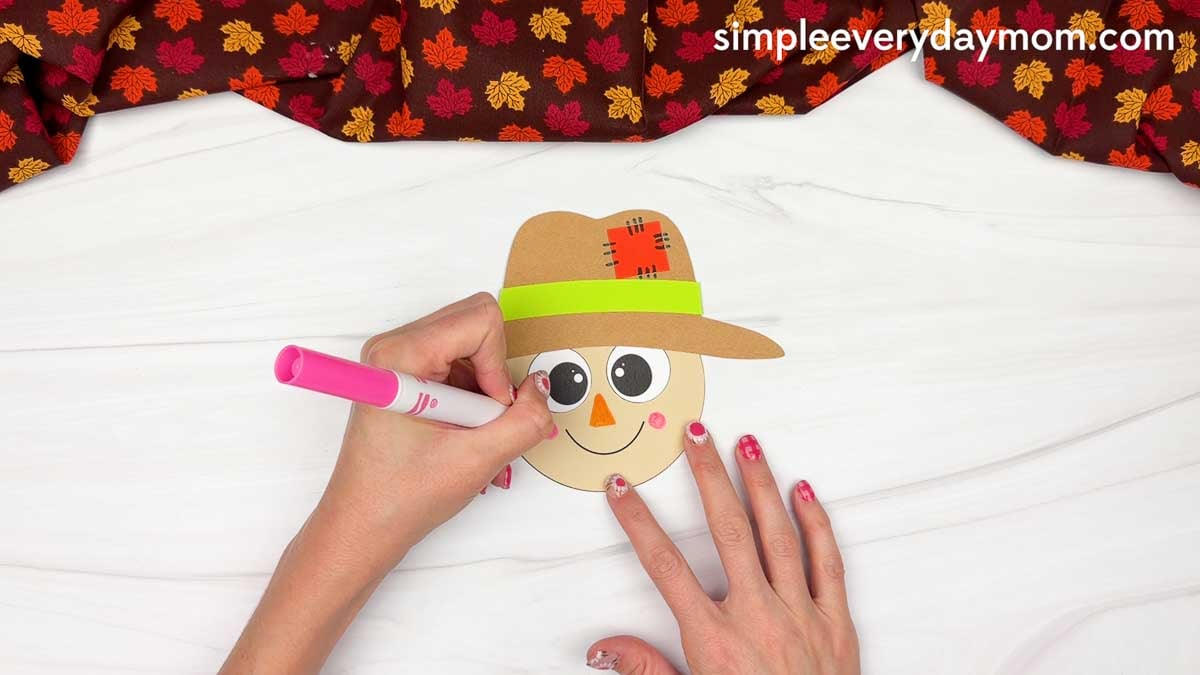 Hands drawing the scarecrow cheeks on both sides of the smile for the Fork Painted Scarecrow Craft.