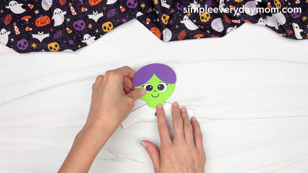 Hands gluing the witch’s head onto the top of the body.