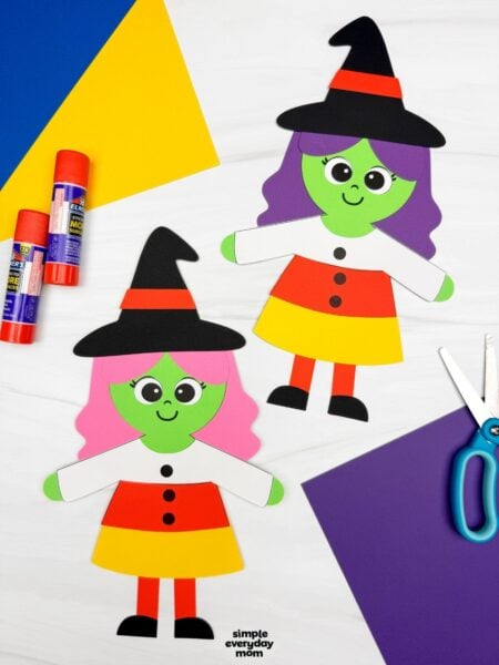 A completed craft showing two Witch Candy Corn Crafts with witch hats, colorful hair, and candy corn dresses alongside craft supplies.