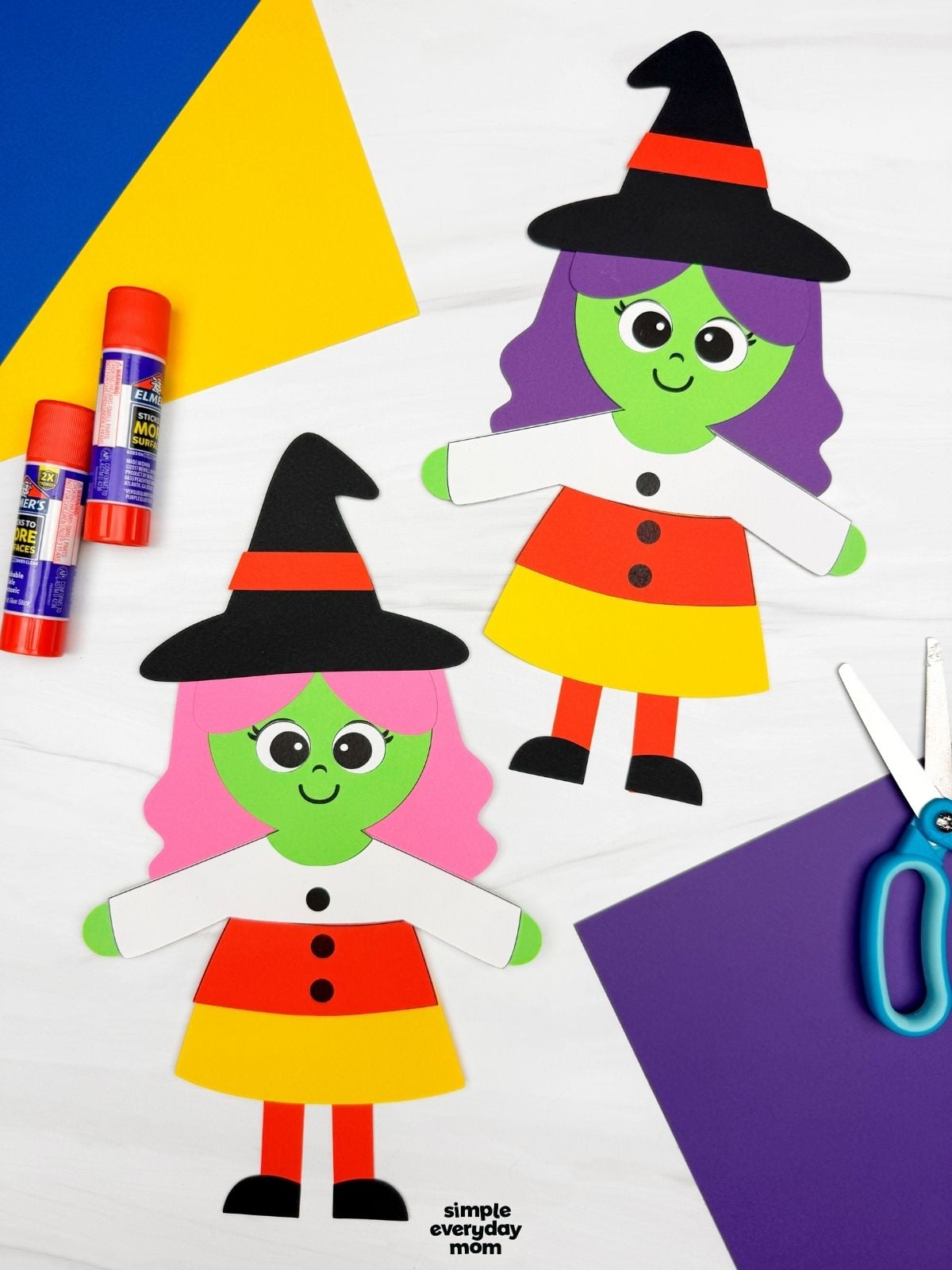 A completed craft showing two Witch Candy Corn Crafts with witch hats, colorful hair, and candy corn dresses alongside craft supplies.