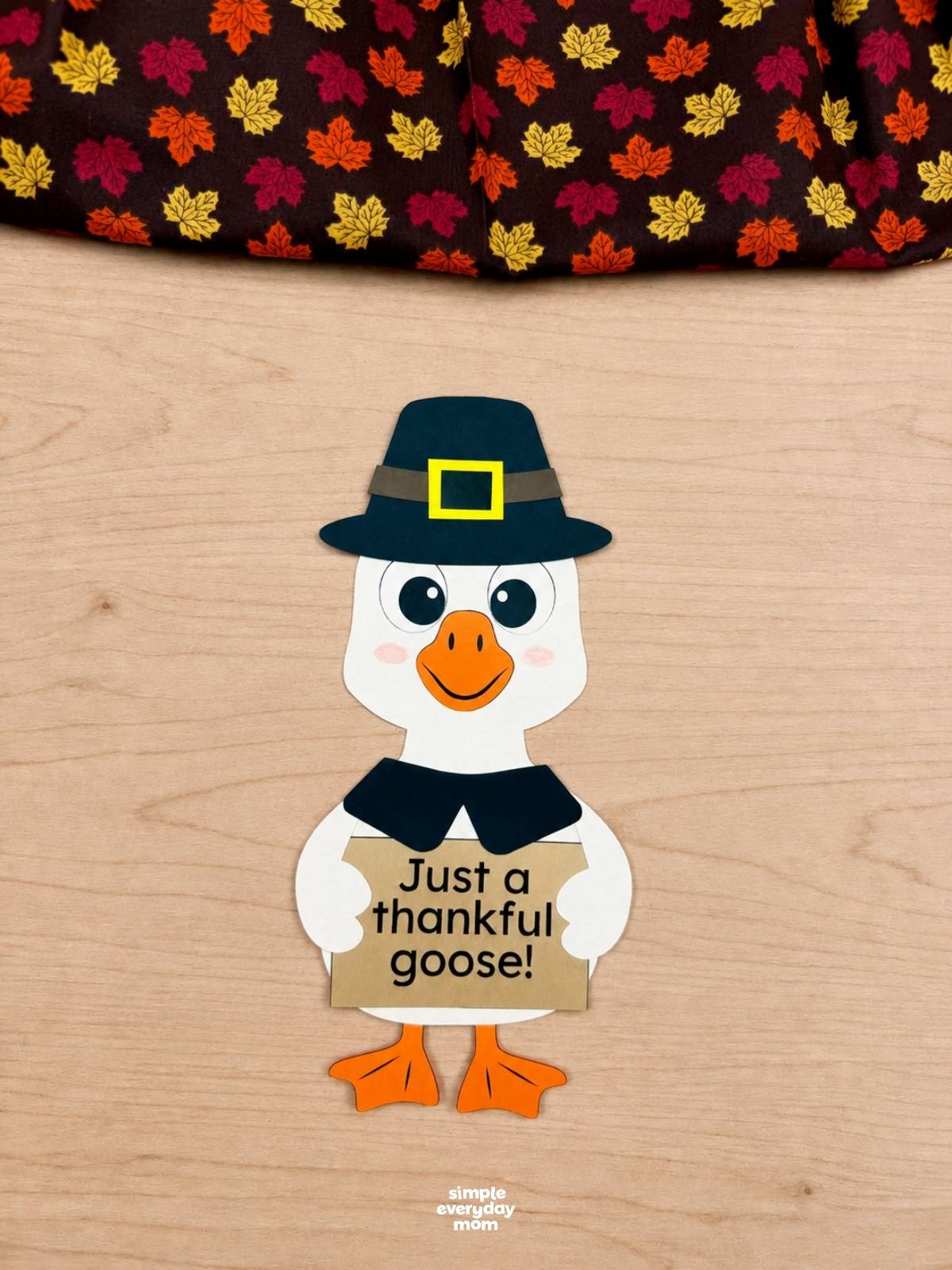 A completed craft of a thankful goose wearing a pilgrim hat and holding a sign that says "Just a thankful goose!"