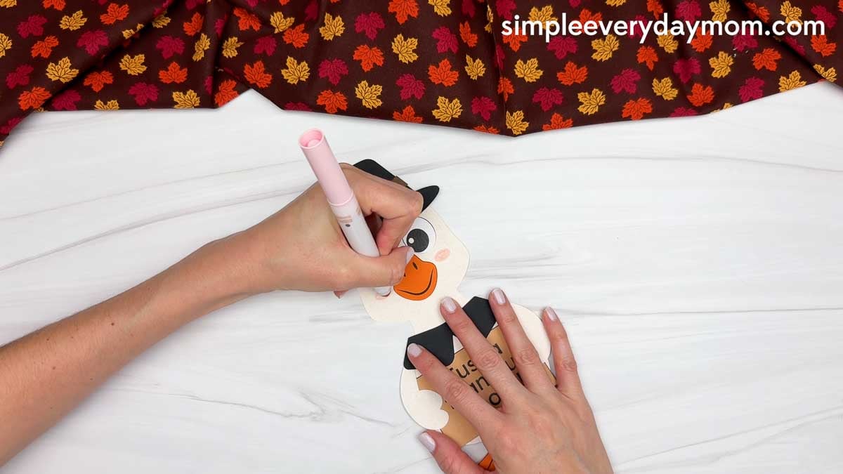 Hands using a pink marker to add rosy cheeks to the Thankful Goose Craft for Thanksgiving.