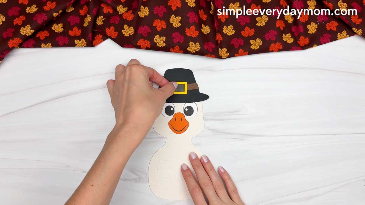 Hands gluing a yellow buckle onto the black pilgrim hat of the Thankful Goose Craft.