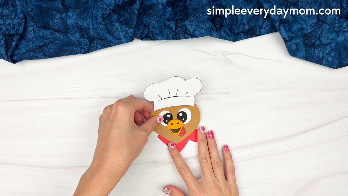 hands assembling the chef turkey disguise craft with a white chef hat and uniform.