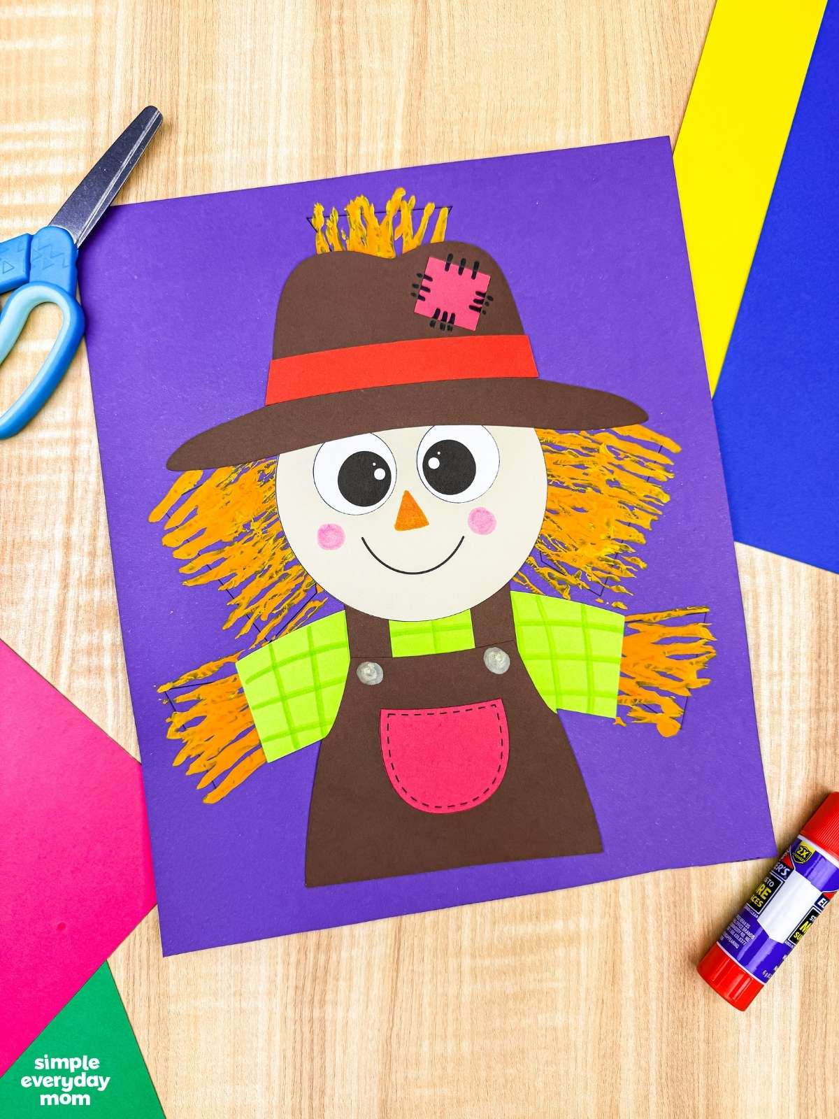A completed craft of a Fork Painted Scarecrow Craft with a painted straw background displayed on a purple sheet of paper.