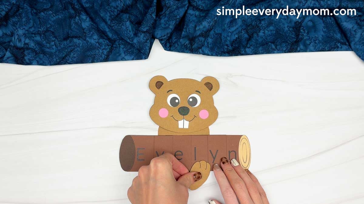 Hands gluing the beaver’s arms onto the name log for the Beaver Name Craft.