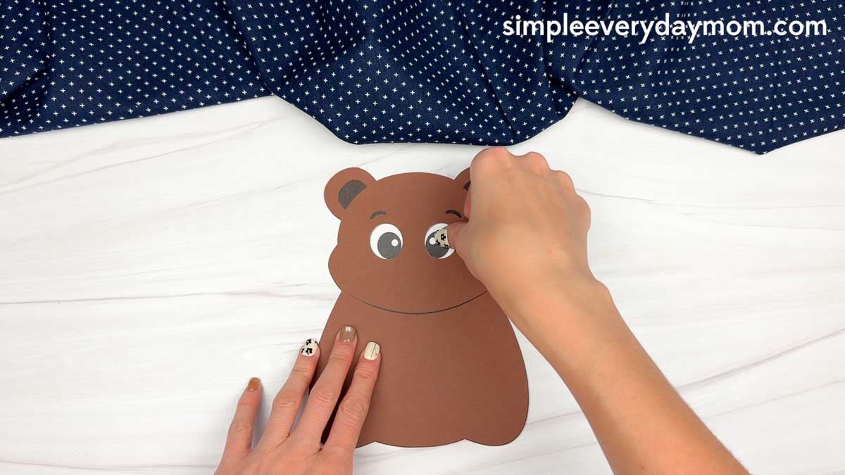 hands attaching an eye piece to a brown paper bear craft.