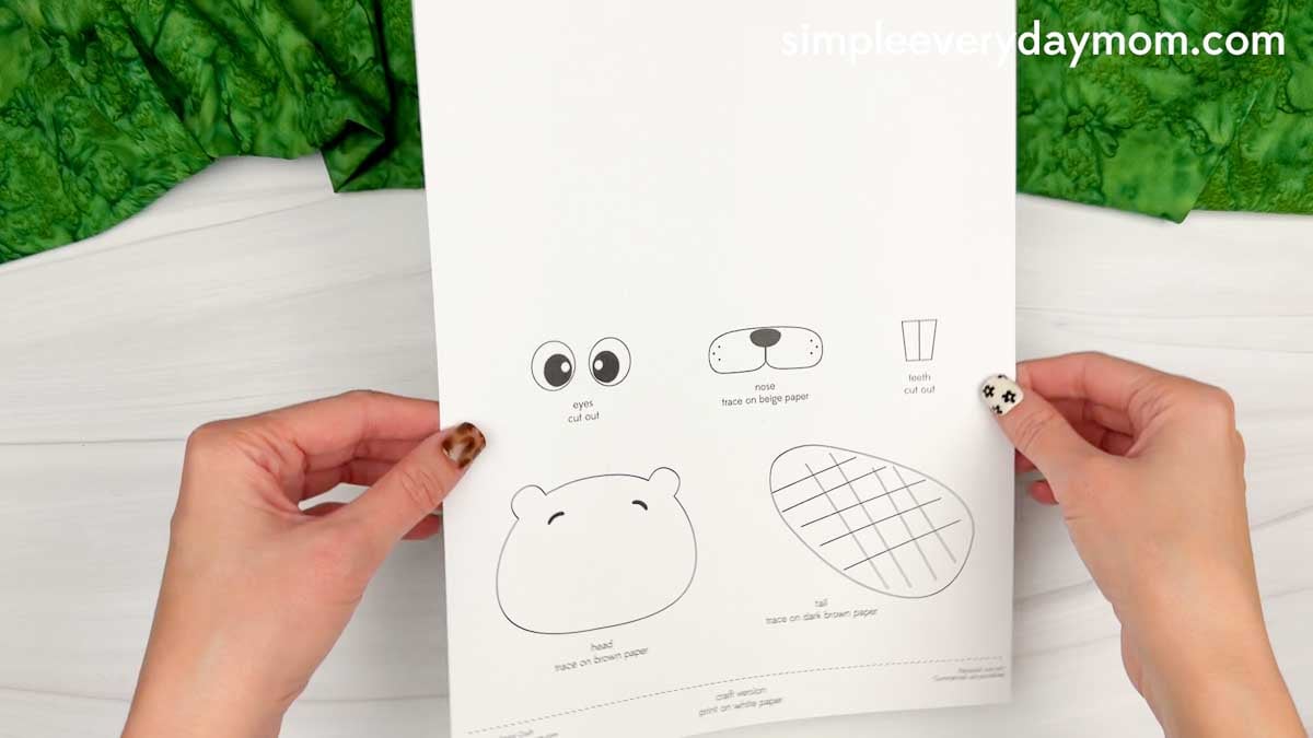 Hands holding a Beaver Handprint Craft template showing the head, eyes, nose, teeth, and tail pieces.