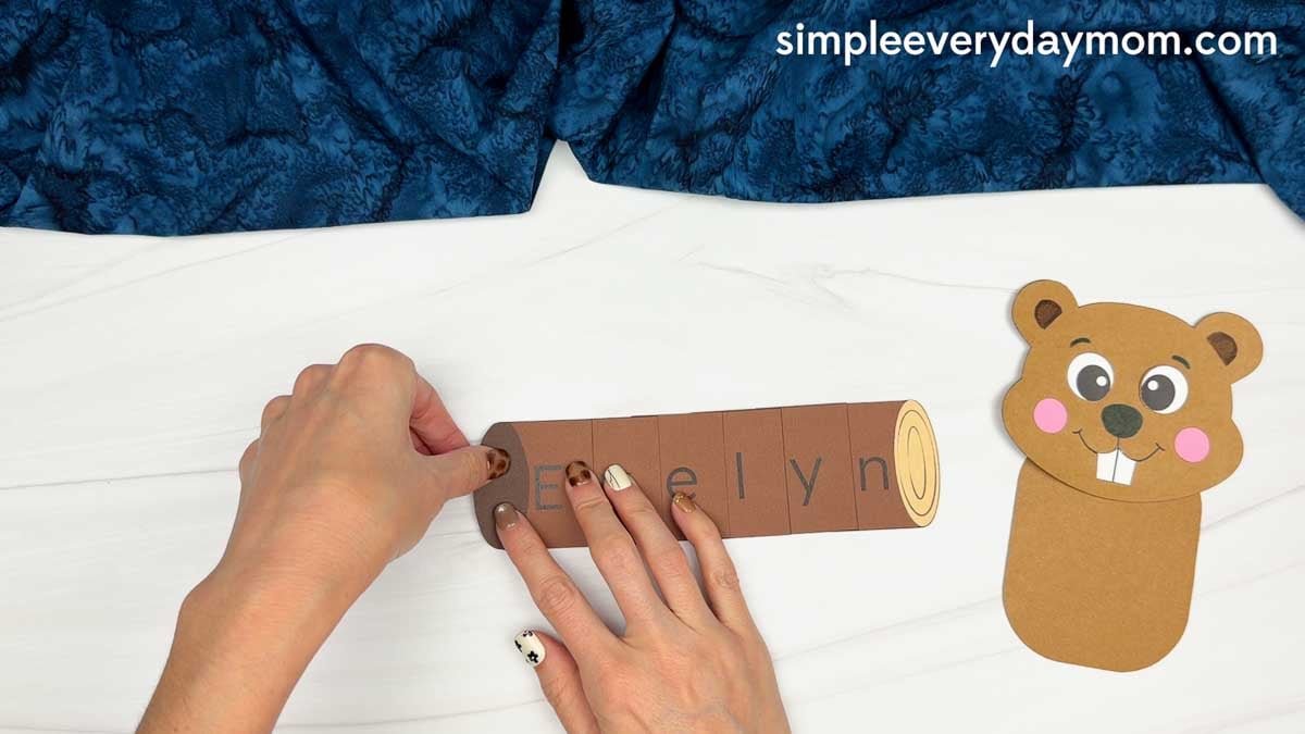 Hands gluing the left end of the log onto the name pieces for the Beaver Name Craft.