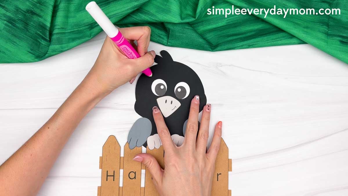 Hands using a marker to add details to the crow’s head above the personalized name fence.