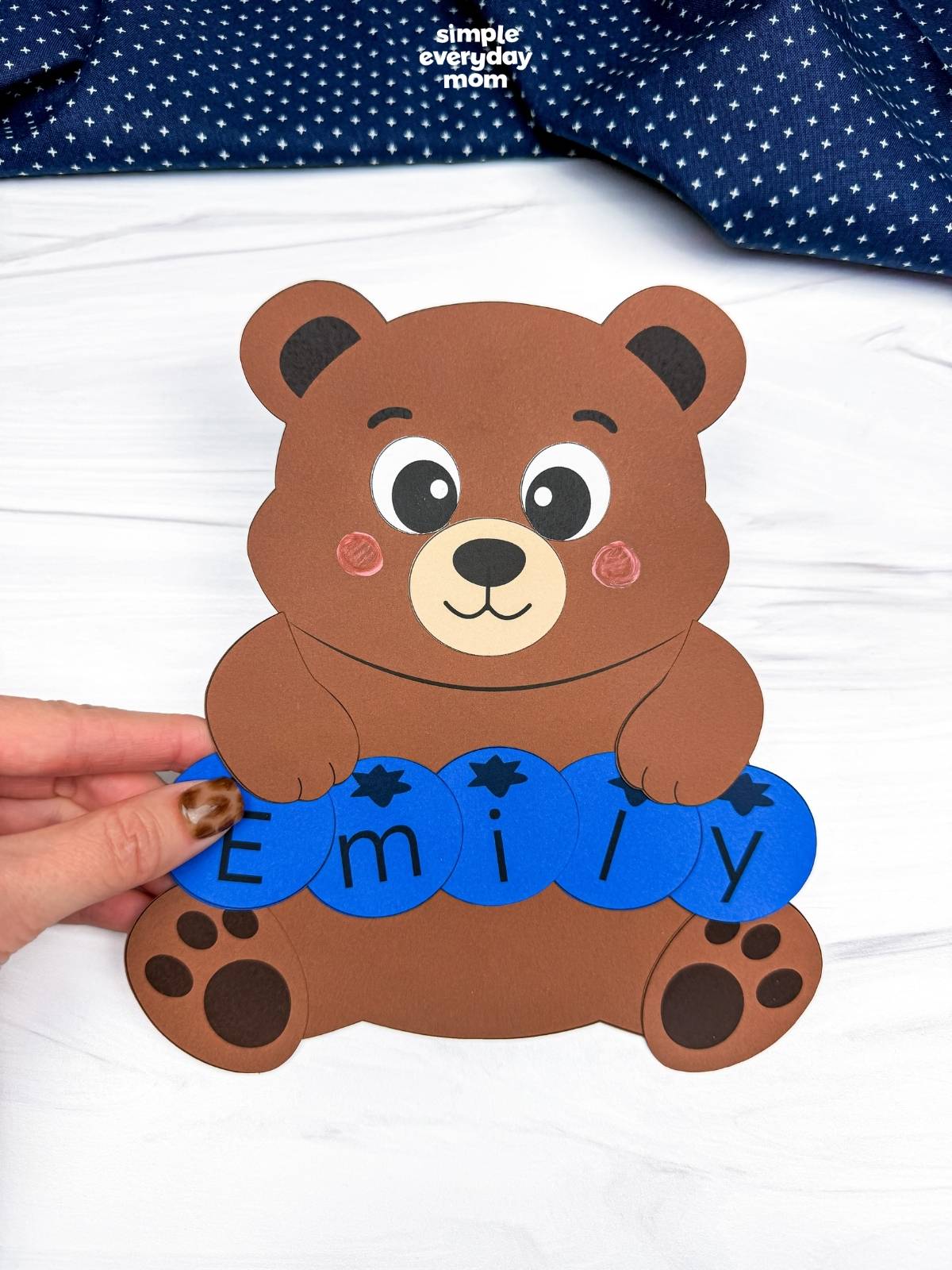 hands holding a completed brown bear name craft with blue letter pieces spelling Emily.