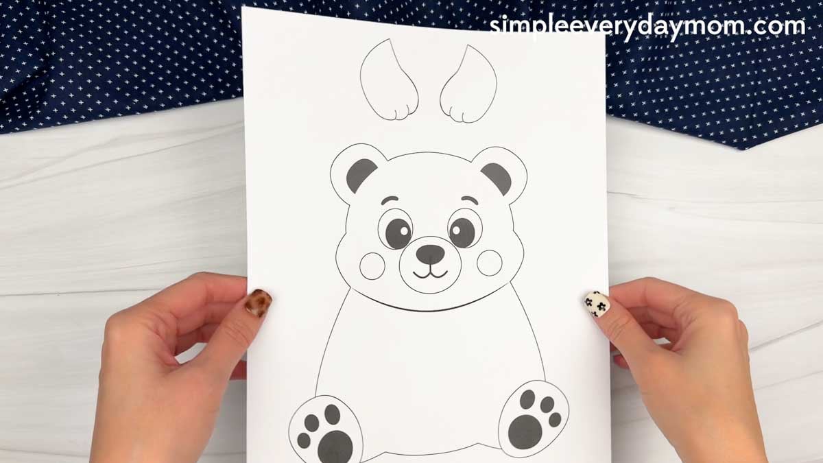 hands holding a printable bear craft template with a bear body, face, paws, and arms.