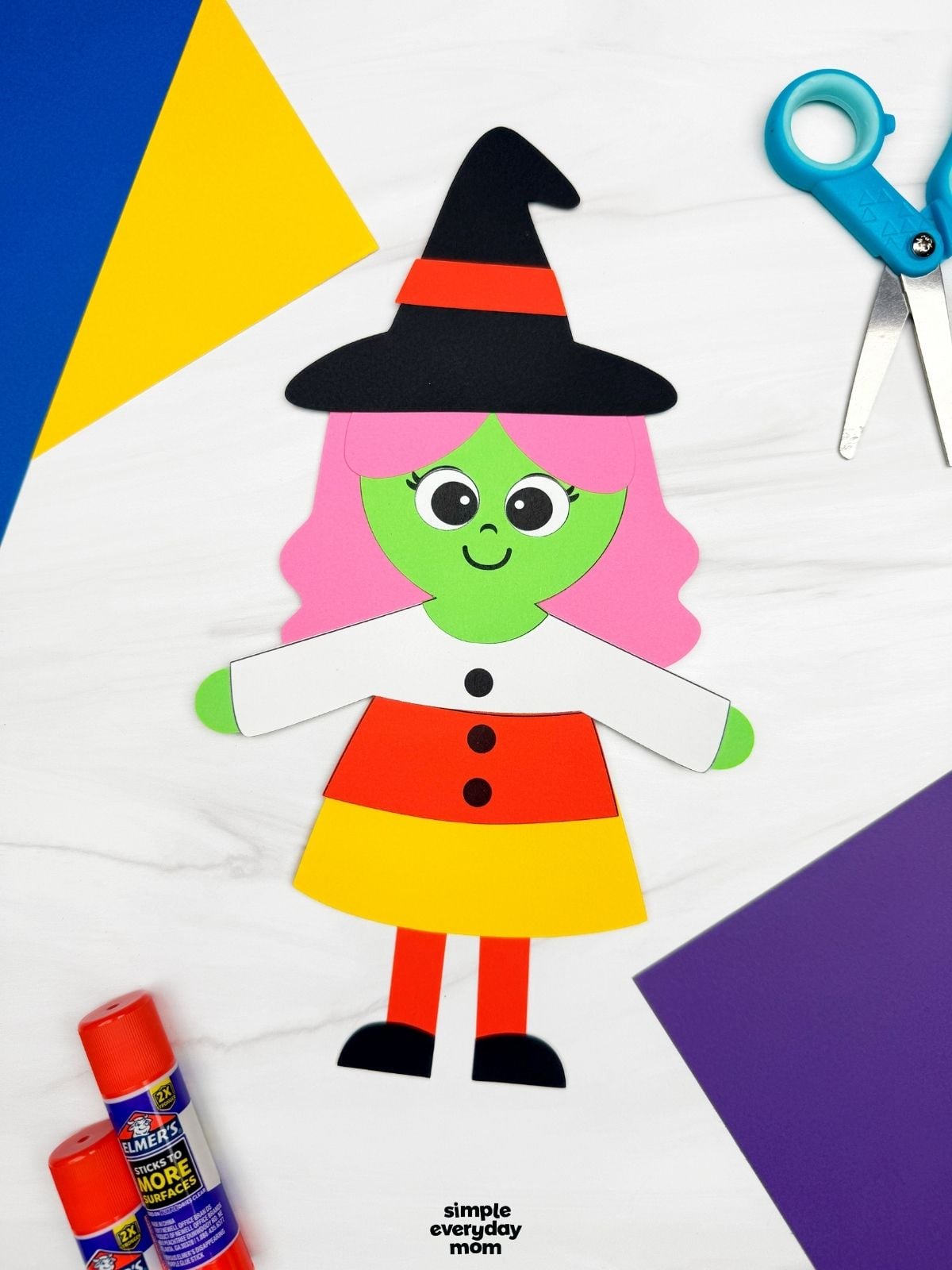 A completed craft showing a Witch Candy Corn Craft with pink hair, a witch hat, and a candy corn dress alongside craft supplies.