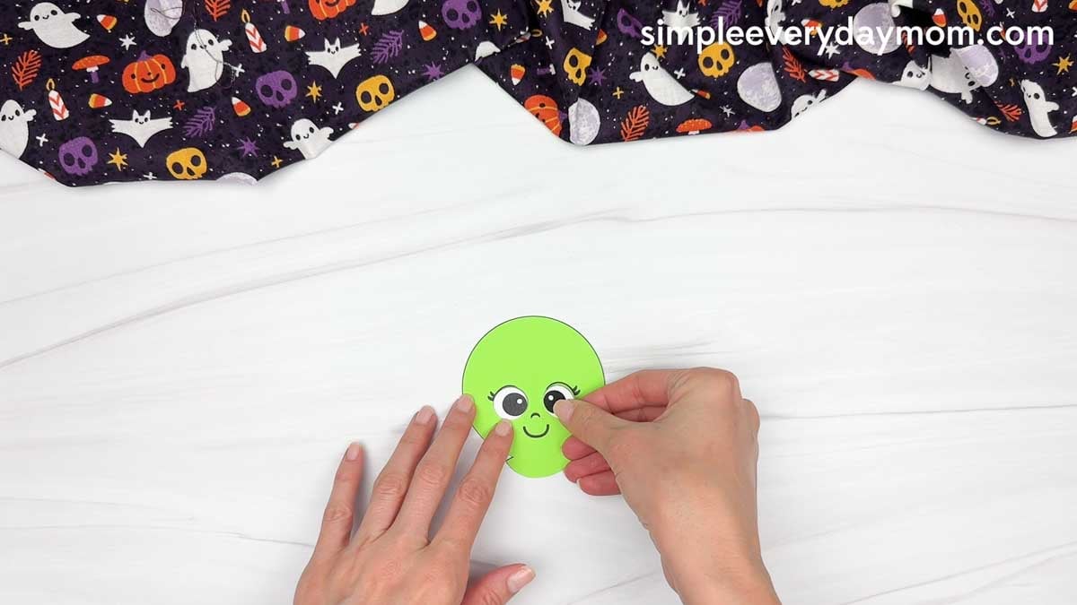 Hands gluing an eye onto the witch’s green face for the Witch Candy Corn Craft.