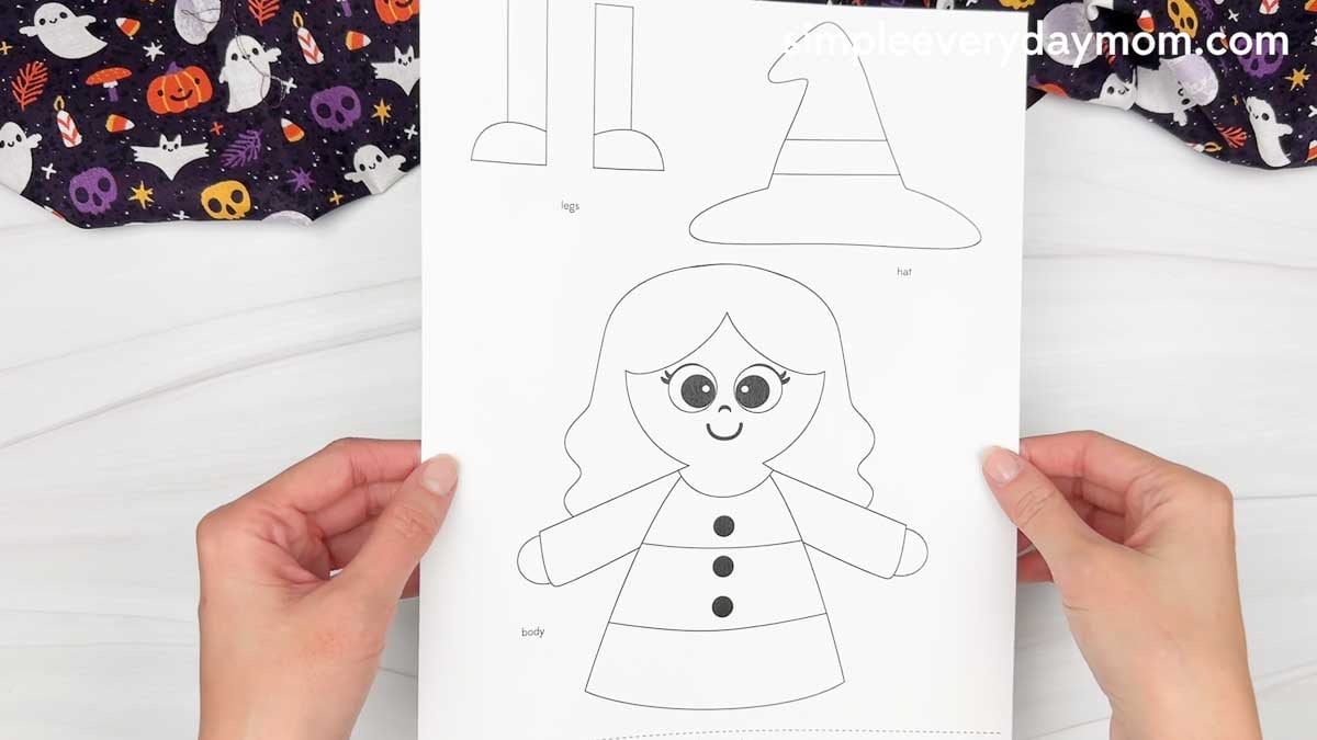 Hands holding a printable Witch Candy Corn Craft template featuring the witch body, hat, and legs.