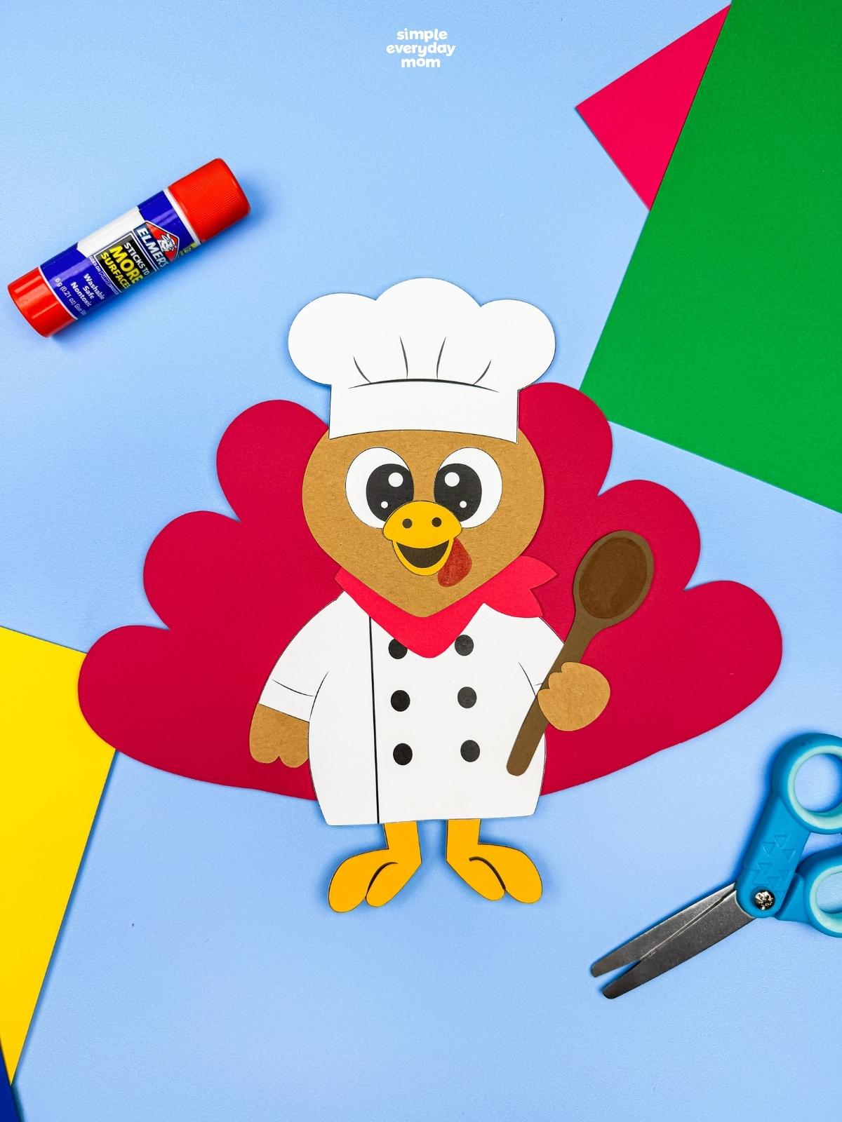 A completed Craft featuring a chef turkey disguise with red tail feathers, a white chef uniform, and a brown spoon.