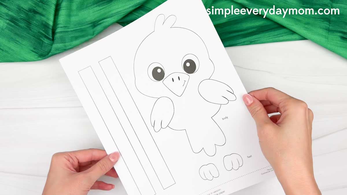 Hands holding a printable crow name craft template with the crow body, feet, and name strip pieces.