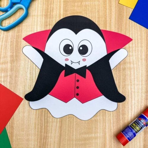 A completed craft of the Vampire Ghost Disguise Craft displayed with colorful paper, scissors, and a glue stick.