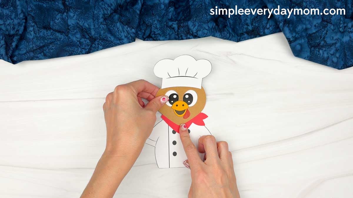 hands assembling the chef turkey disguise craft with a white chef coat and red neckerchief.