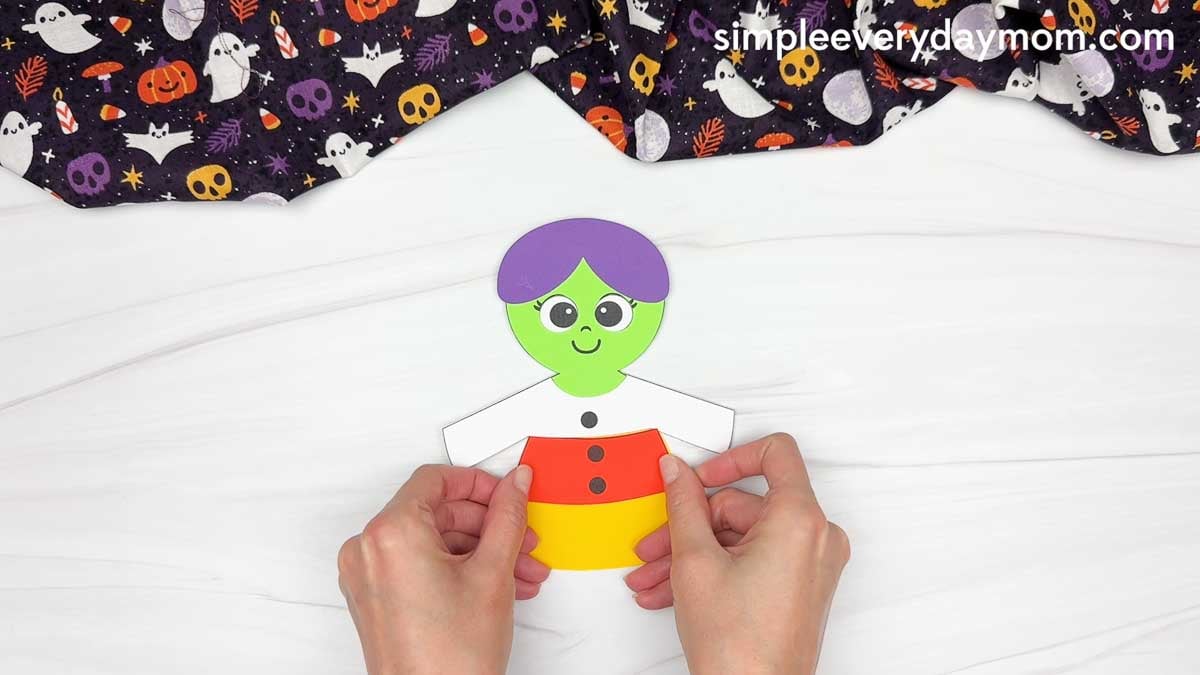 Hands attaching the candy corn dress pieces to the witch’s body.