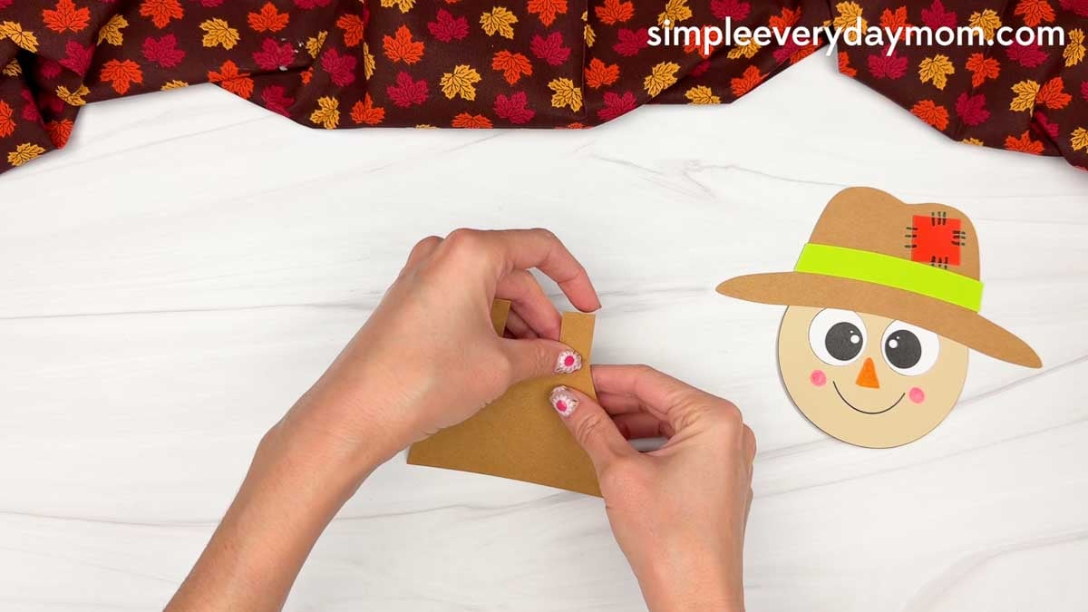 Hands gluing the button pieces onto the overall straps for the Fork Painted Scarecrow Craft.