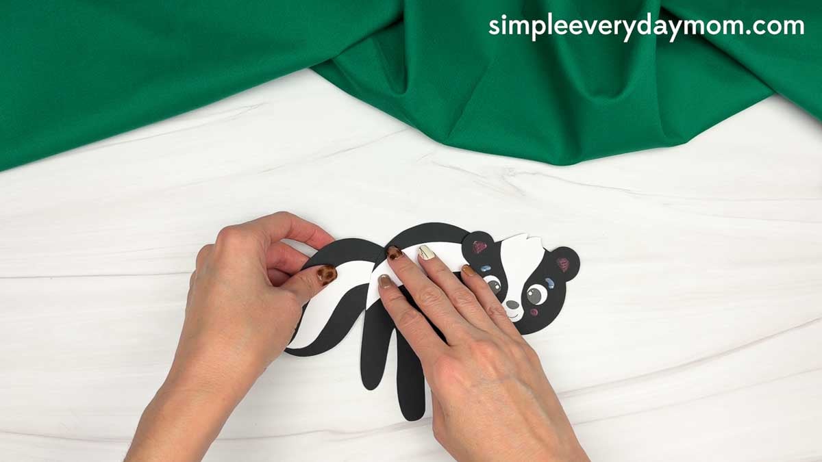 hands attaching the black and white tail to the skunk handprint craft.