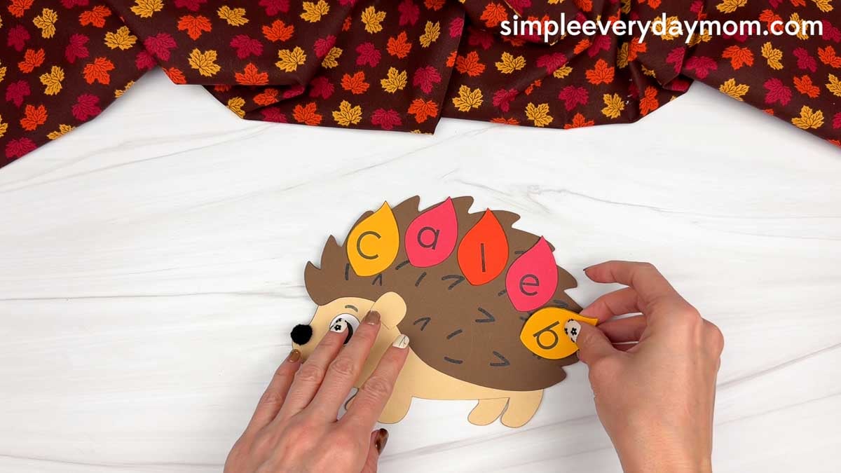 Hands attaching the final lettered leaf to the hedgehog’s back to complete the name.