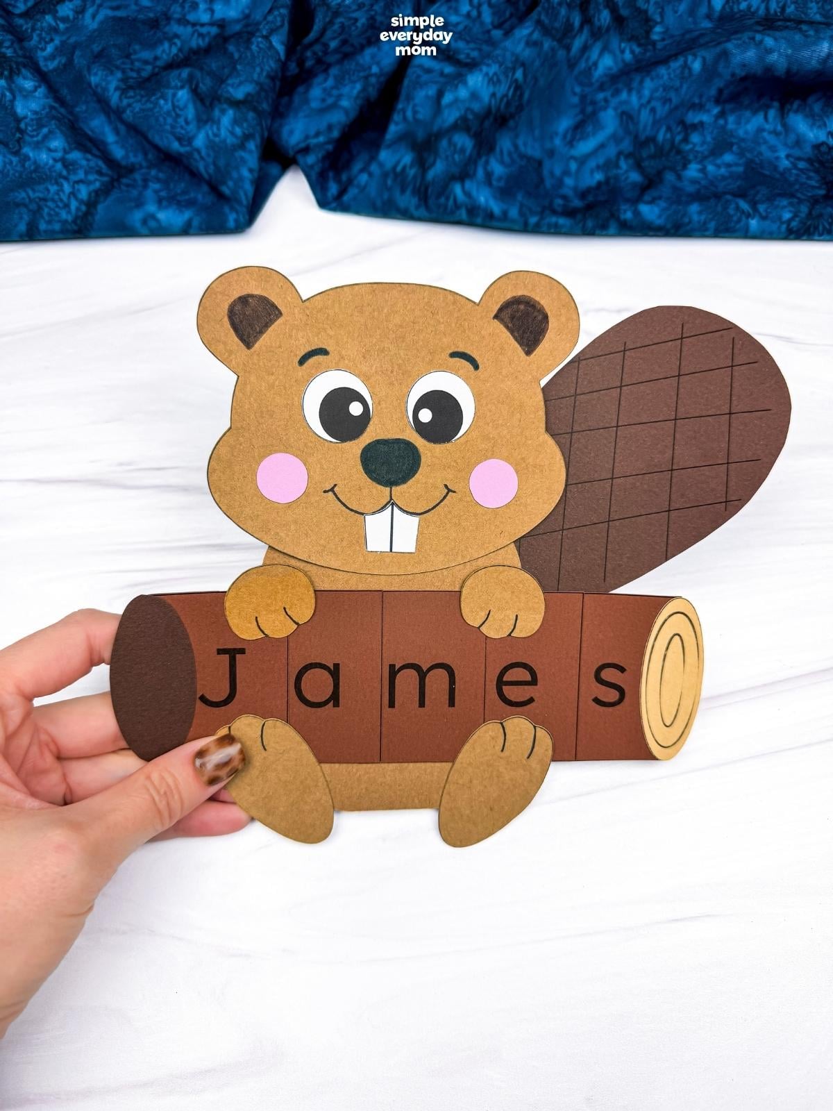 Hands holding a completed Beaver Name Craft with a beaver holding a log that spells James.