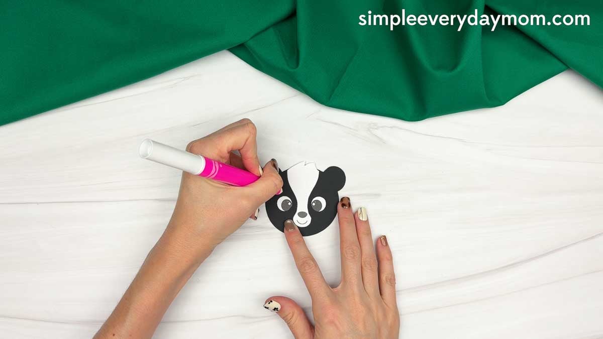 hands using a pink marker to add details to the skunk face cutout.