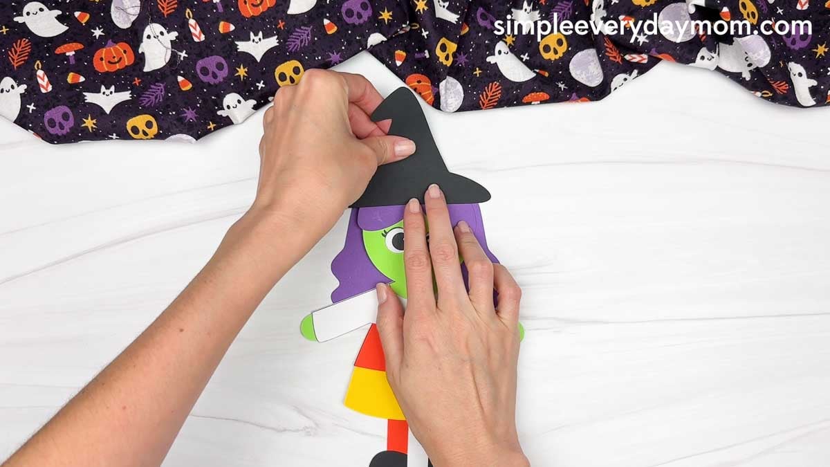 Hands attaching the witch hat to the top of the witch’s head.
