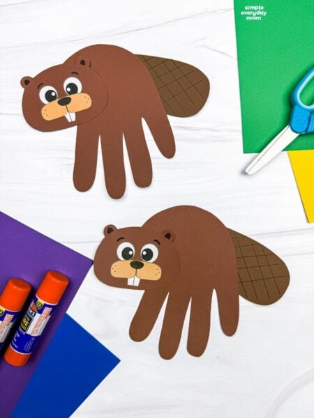 A completed Beaver Handprint Craft displayed with paper, scissors, and glue sticks.