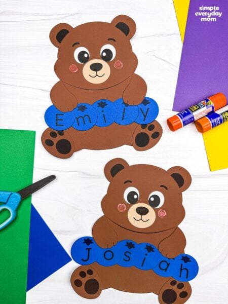 A completed Craft featuring two brown bear name crafts with blue letter pieces spelling Emily and Josiah, surrounded by colorful craft supplies.