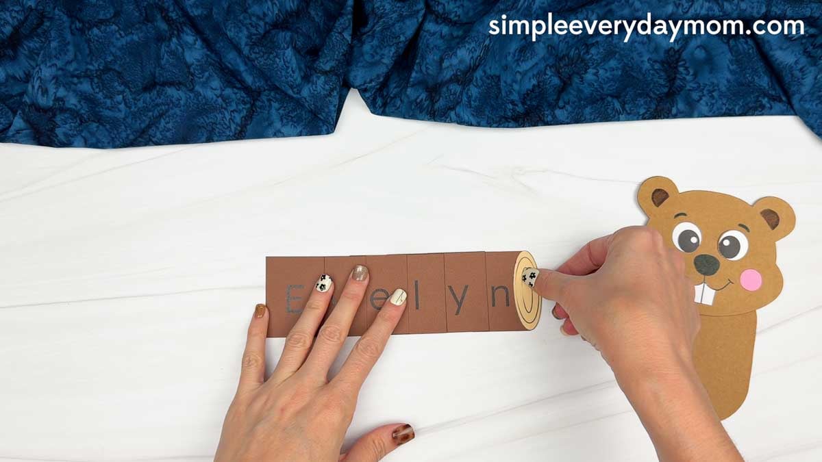 Hands gluing the right end of the log onto the name pieces for the Beaver Name Craft.