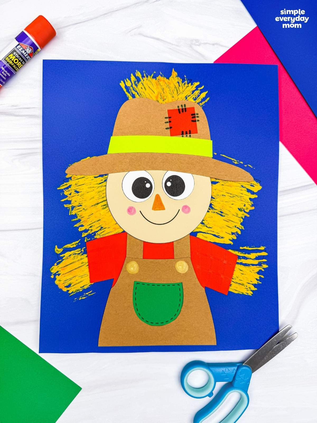 A completed craft of a Fork Painted Scarecrow Craft with a painted straw background displayed on a sheet of paper.