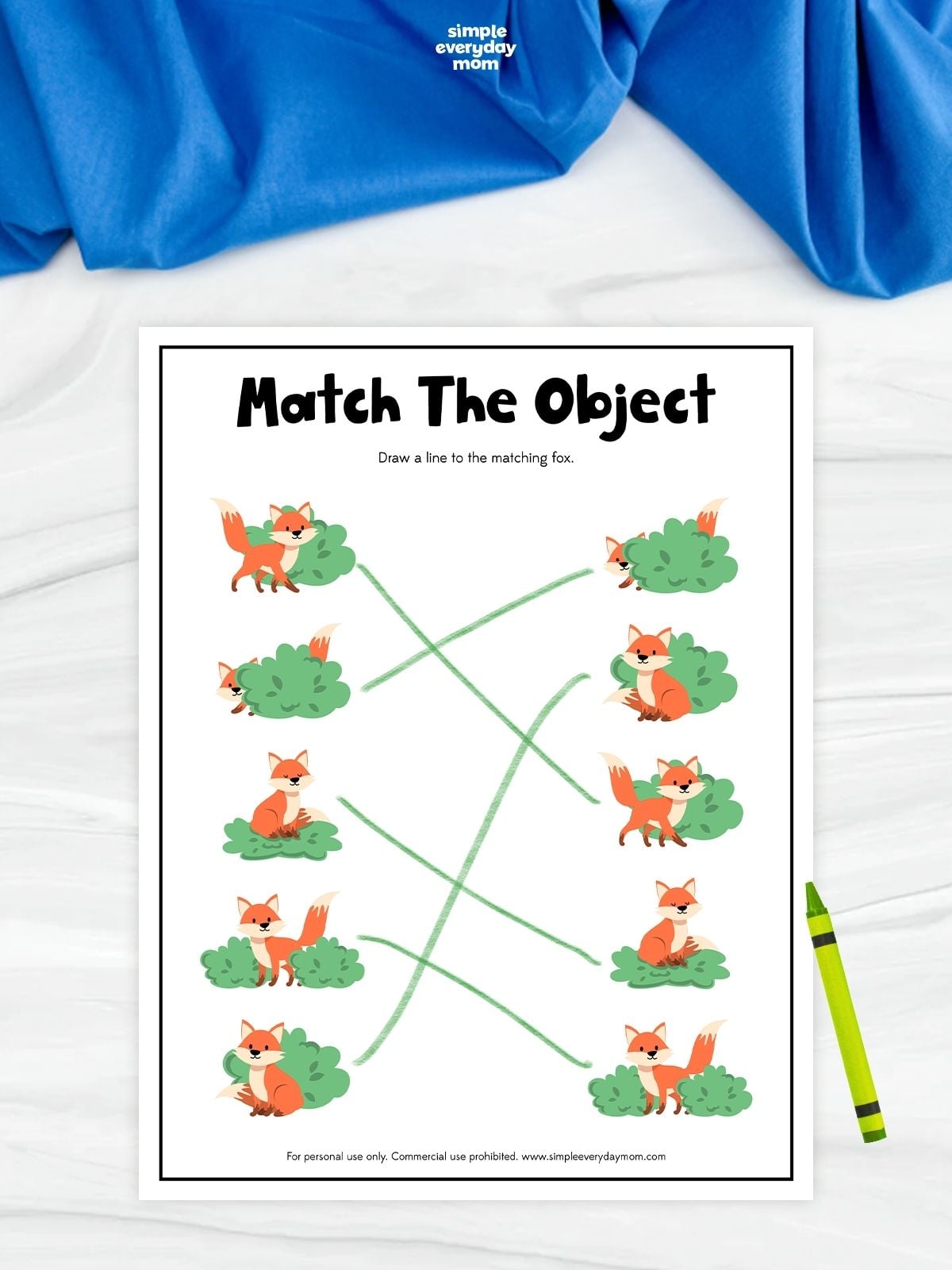 A fox object matching worksheet with pairs of foxes posed beside green bushes. Children draw lines to connect each fox scene with its identical matching picture. A green crayon rests beside the completed worksheet.