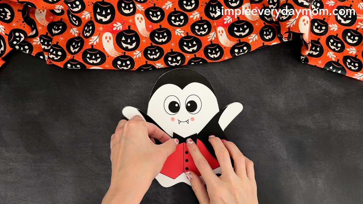 Hands gluing the bow tie to the top center of the vampire vest on the Vampire Ghost Disguise Craft.