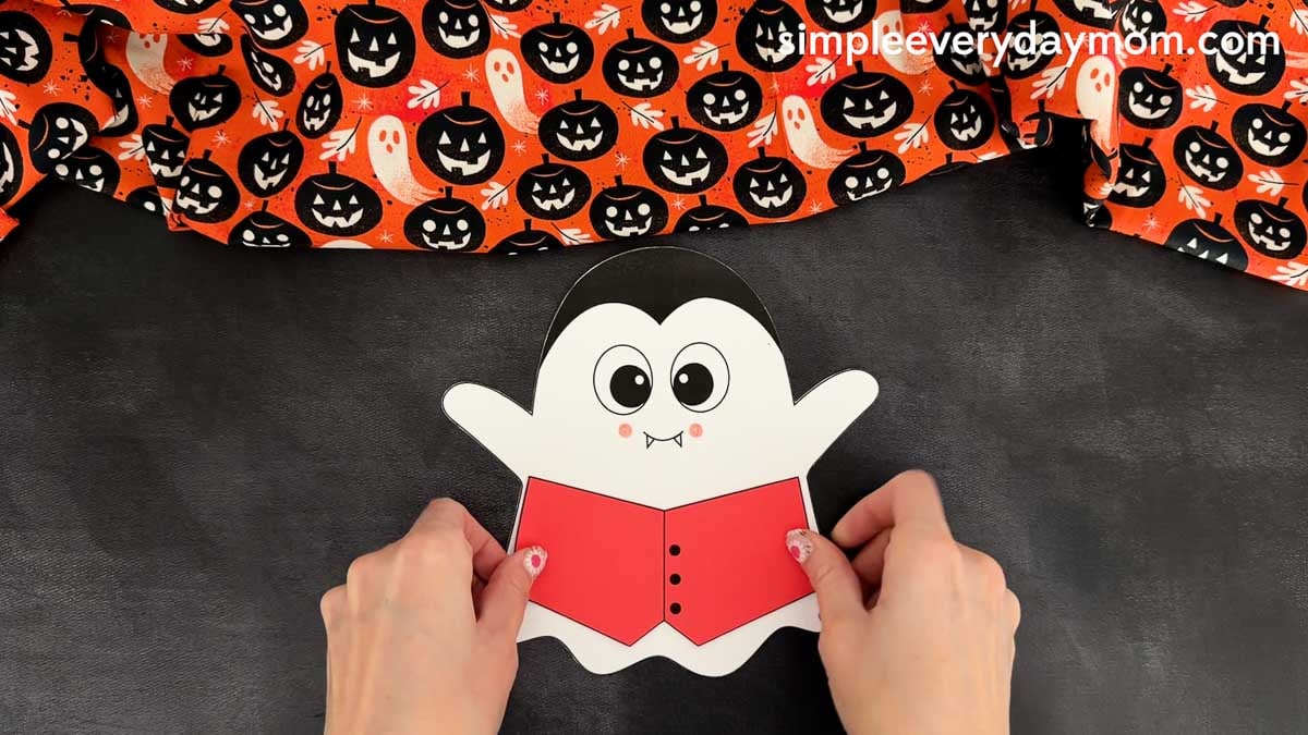 Hands gluing the vampire vest onto the center of the ghost body for the Vampire Ghost Disguise Craft.