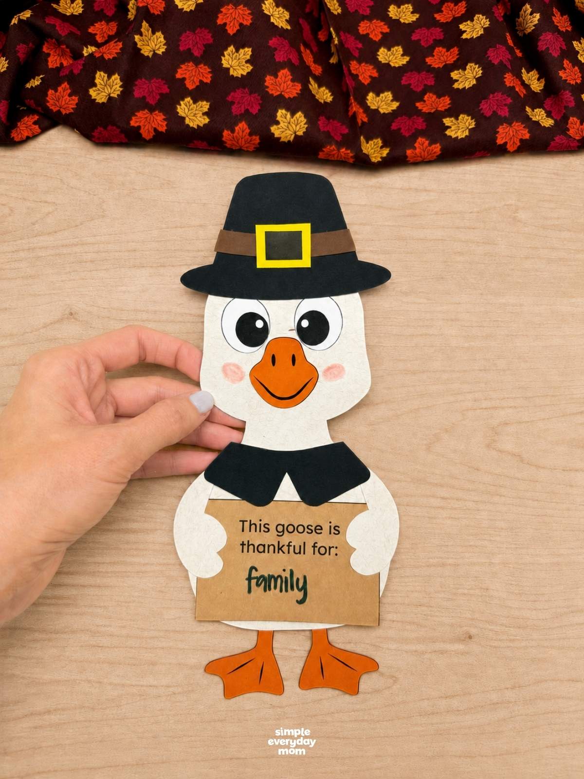 Hands holding a completed Thankful Goose Craft wearing a pilgrim hat and holding a gratitude sign that says family.