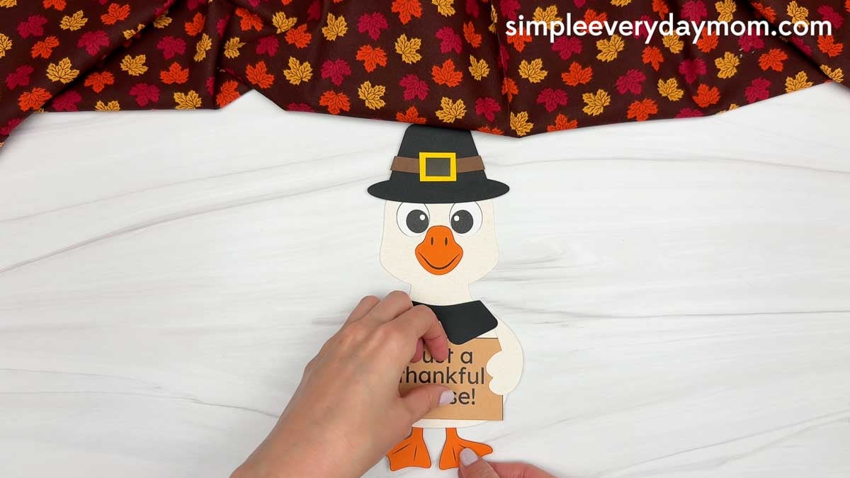Hands gluing orange feet to the bottom of the Thankful Goose Craft for Thanksgiving.