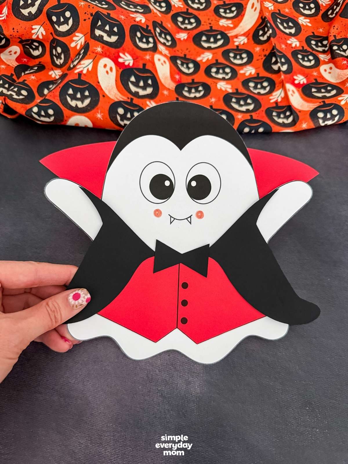 Hands holding the completed Vampire Ghost Disguise Craft featuring a vampire cape, collar, bow tie, and vest.