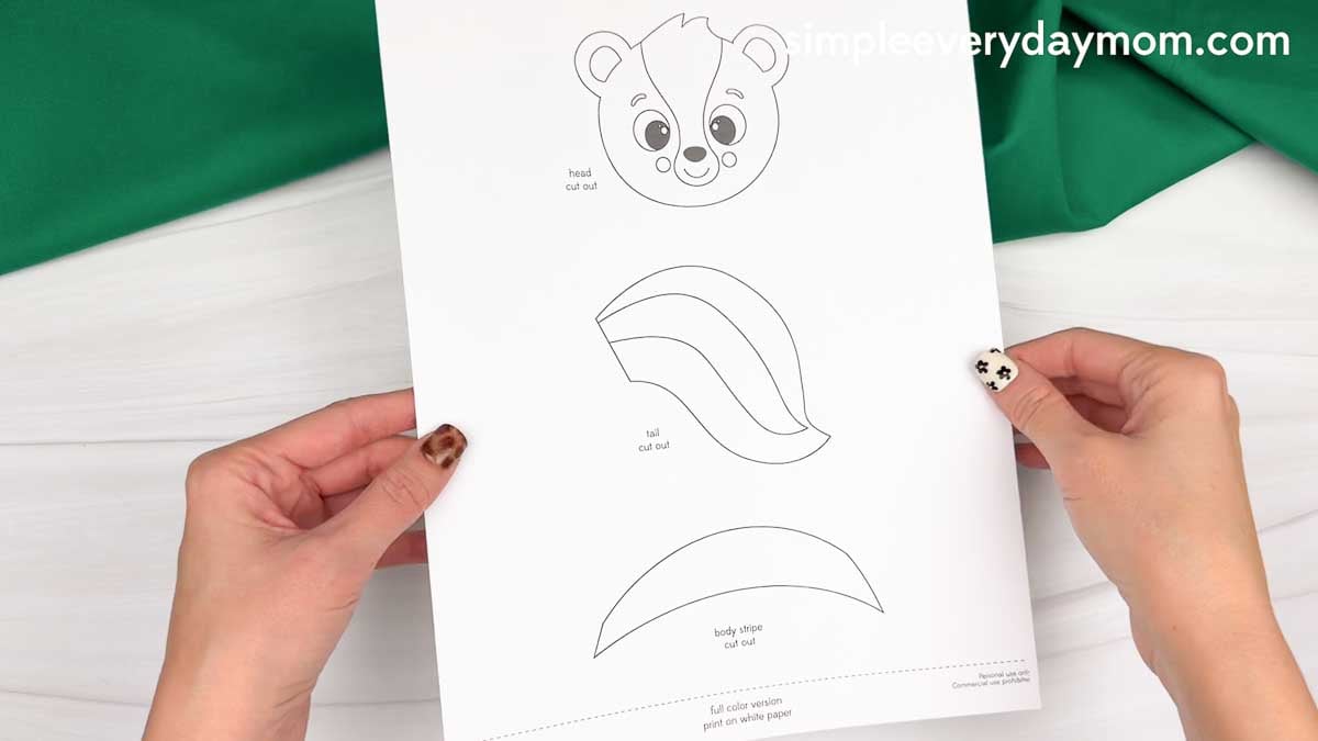 hands holding a printable skunk craft template with head, tail, and body stripe pieces.