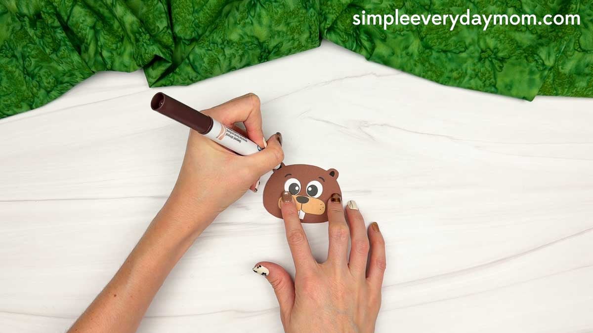 Hands drawing details on the beaver head with a marker.