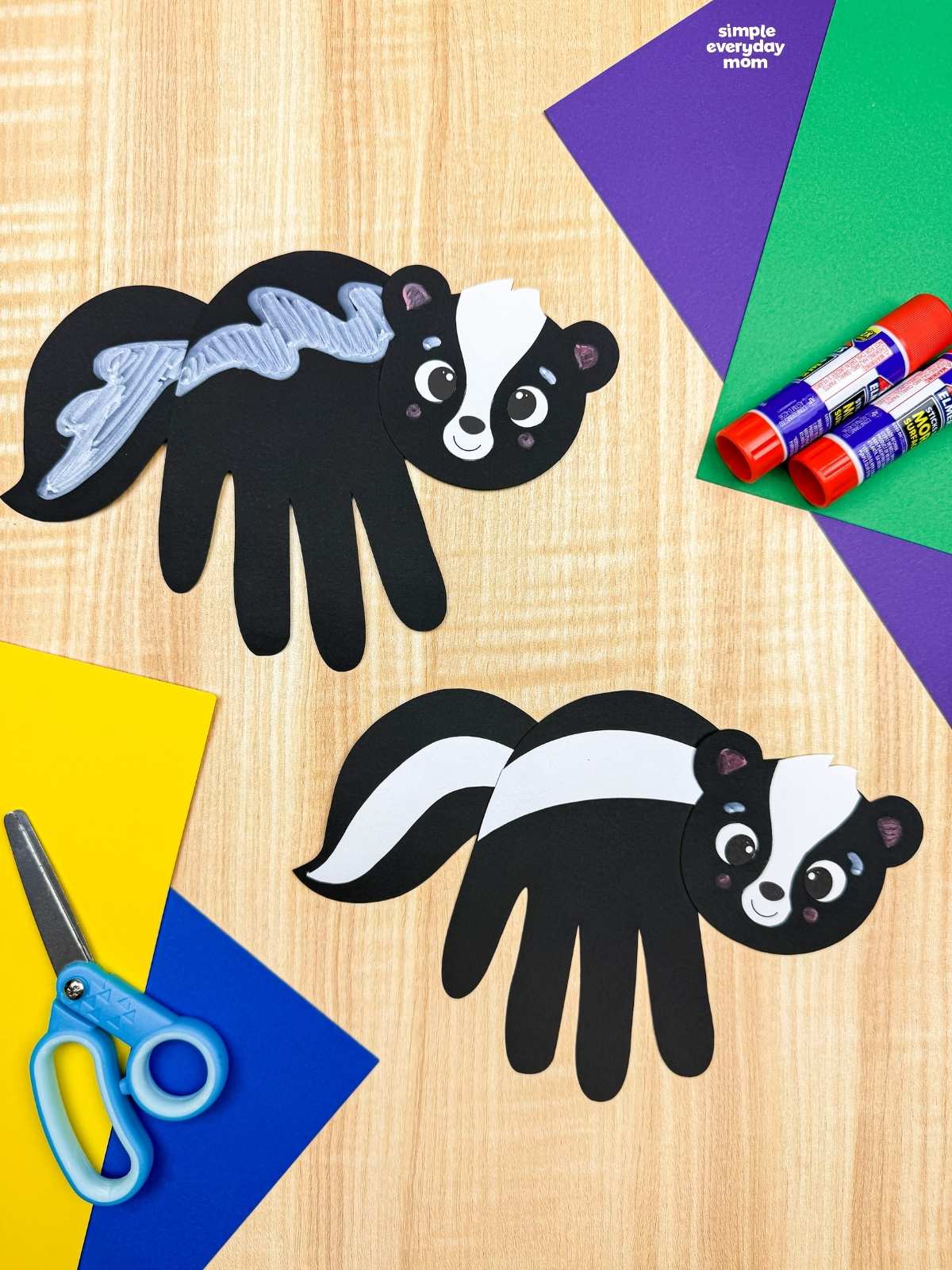A completed Craft featuring two black handprint skunks with white and silver stripes surrounded by colorful craft supplies.